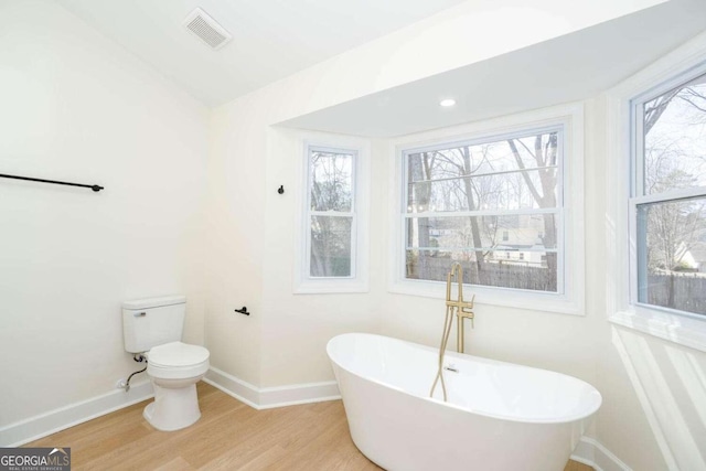 bathroom with hardwood / wood-style flooring, a tub, plenty of natural light, and toilet