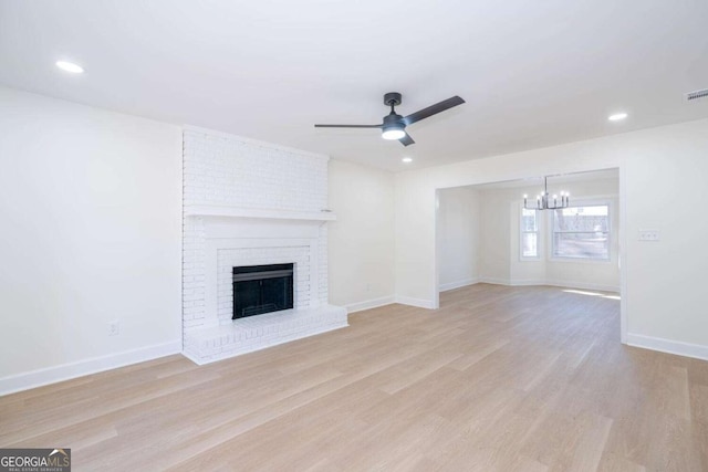 unfurnished living room featuring a brick fireplace, ceiling fan with notable chandelier, and light hardwood / wood-style floors