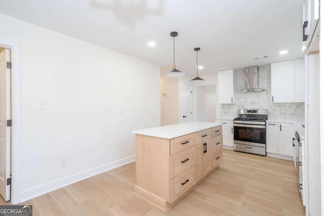 kitchen with wall chimney range hood, stainless steel gas stove, white cabinetry, a center island, and decorative backsplash