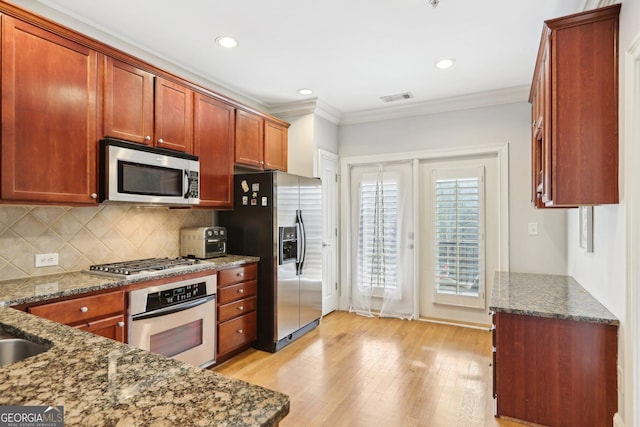 kitchen featuring crown molding, dark stone countertops, stainless steel appliances, light hardwood / wood-style floors, and decorative backsplash