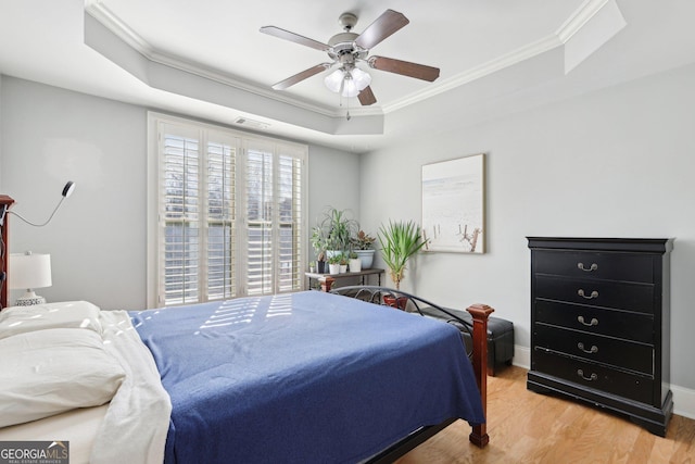 bedroom with crown molding, a tray ceiling, ceiling fan, and light wood-type flooring