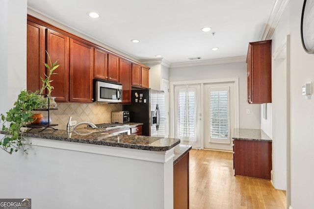 kitchen featuring stainless steel appliances, crown molding, dark stone countertops, and kitchen peninsula