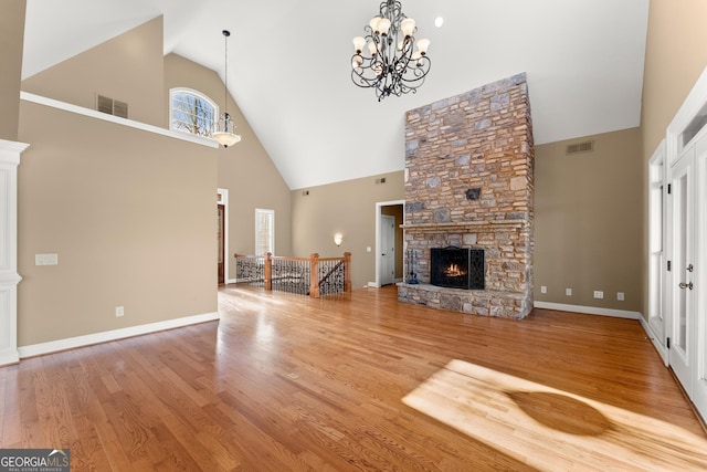 unfurnished living room featuring a stone fireplace, hardwood / wood-style floors, a notable chandelier, and high vaulted ceiling