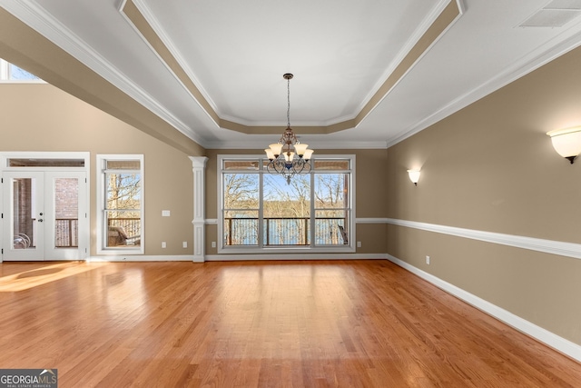 unfurnished dining area featuring a notable chandelier, light hardwood / wood-style flooring, decorative columns, and a raised ceiling