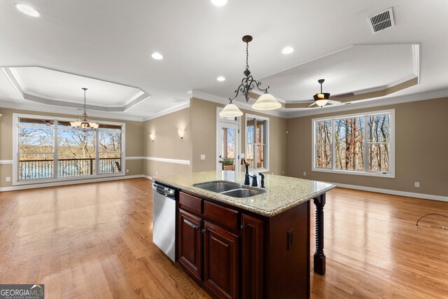 kitchen with sink, light stone counters, decorative light fixtures, a raised ceiling, and a kitchen island with sink