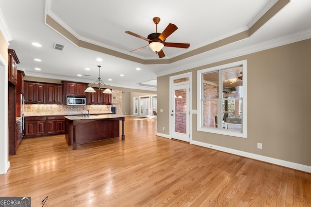 kitchen with pendant lighting, light hardwood / wood-style flooring, light stone countertops, a center island with sink, and a raised ceiling