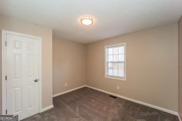 spare room featuring a textured ceiling and dark colored carpet