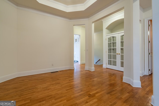 empty room featuring french doors, a tray ceiling, crown molding, and hardwood / wood-style flooring