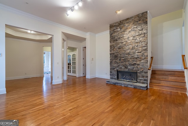 unfurnished living room featuring crown molding, rail lighting, light hardwood / wood-style floors, a stone fireplace, and a raised ceiling