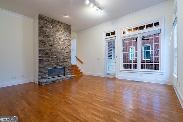 unfurnished living room featuring crown molding, a stone fireplace, track lighting, and hardwood / wood-style flooring