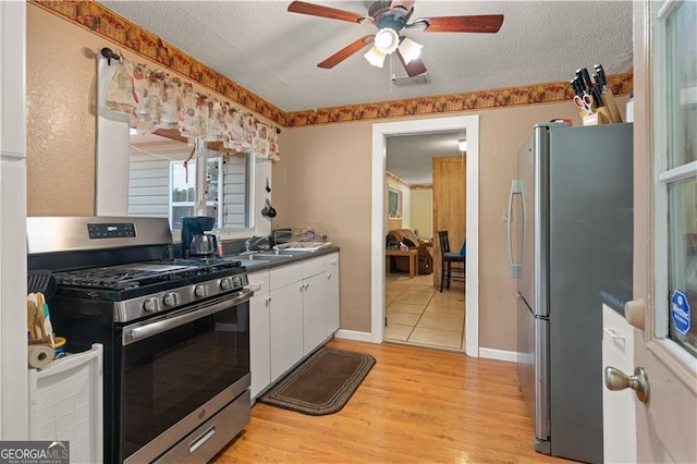 kitchen featuring a textured ceiling, appliances with stainless steel finishes, ceiling fan, light hardwood / wood-style floors, and white cabinets