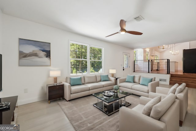 living room with ceiling fan with notable chandelier and light hardwood / wood-style floors