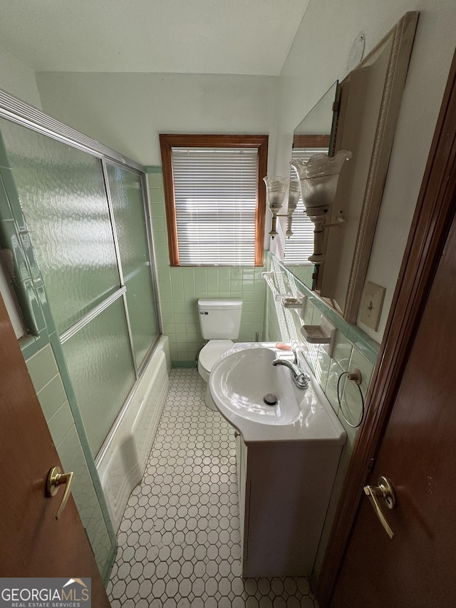 full bathroom with tile walls, vanity, bath / shower combo with glass door, and toilet