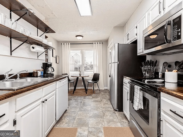 kitchen with appliances with stainless steel finishes, sink, white cabinets, and a textured ceiling