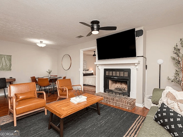 living room featuring a fireplace, dark wood-type flooring, a textured ceiling, and ceiling fan