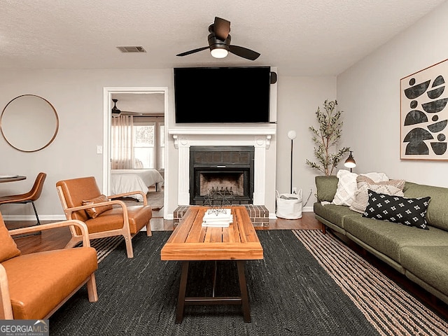 living room featuring ceiling fan, hardwood / wood-style floors, a textured ceiling, and a fireplace