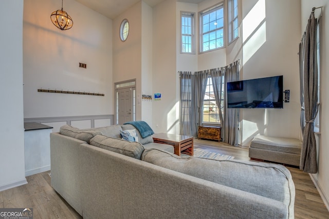 living room with an inviting chandelier, a towering ceiling, light hardwood / wood-style floors, and a wealth of natural light