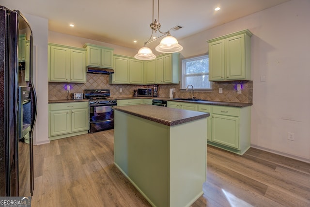 kitchen with sink, black appliances, a kitchen island, decorative light fixtures, and light wood-type flooring