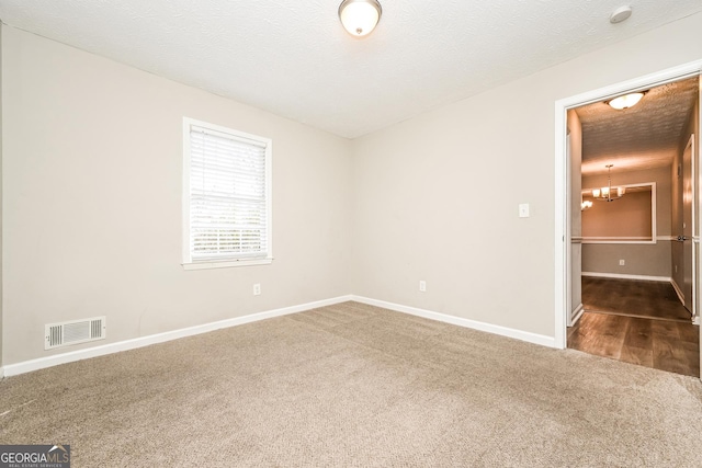 unfurnished room with a chandelier, a textured ceiling, and dark colored carpet