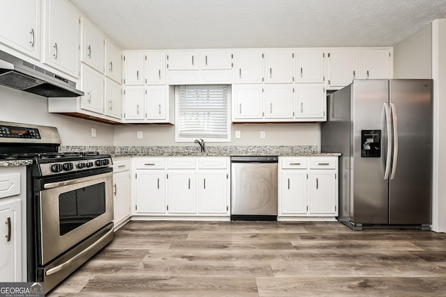 kitchen featuring a textured ceiling, stainless steel appliances, light hardwood / wood-style floors, and white cabinets