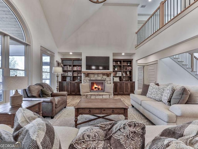 living room with built in shelves, a fireplace, light hardwood / wood-style flooring, and a high ceiling