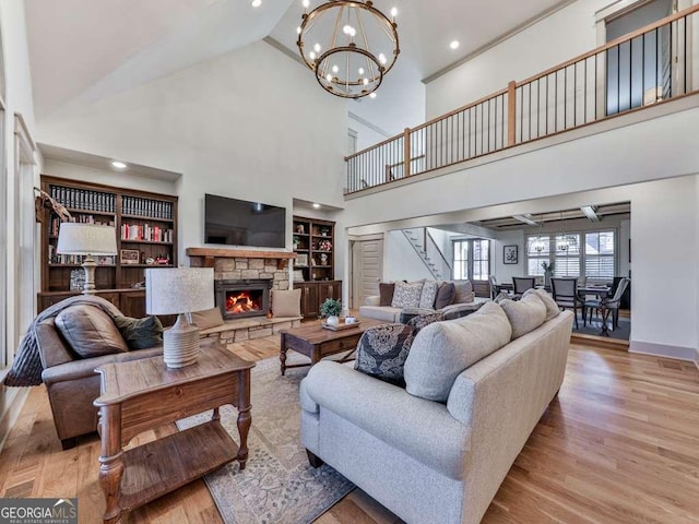 living room with an inviting chandelier, a stone fireplace, light hardwood / wood-style flooring, and built in shelves