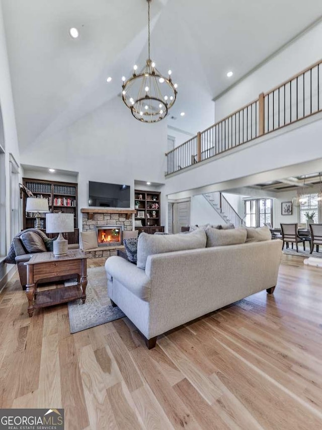 living room with an inviting chandelier, a stone fireplace, light hardwood / wood-style floors, and a towering ceiling