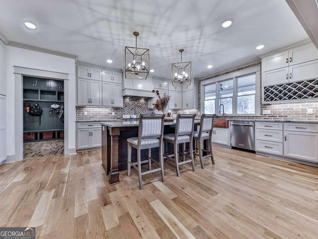 kitchen featuring a breakfast bar area, decorative light fixtures, a center island, dishwasher, and light stone countertops