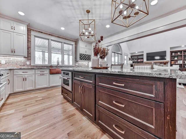 kitchen with hanging light fixtures, plenty of natural light, oven, and white cabinets