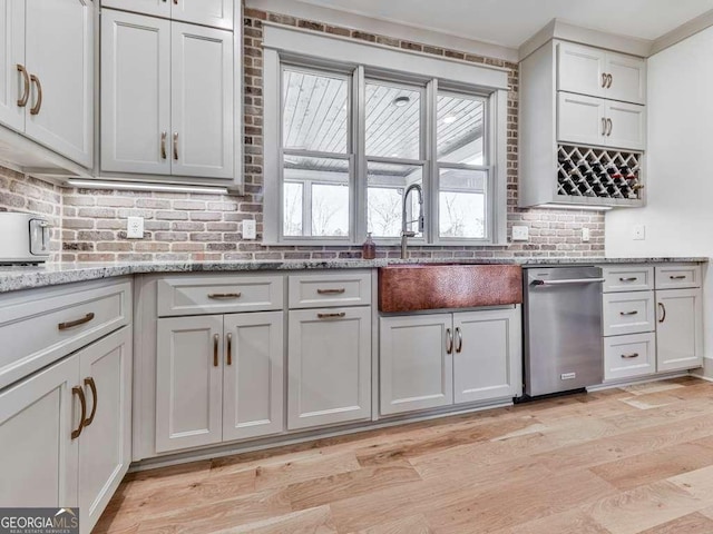 kitchen featuring white cabinetry, sink, stainless steel dishwasher, light stone counters, and light hardwood / wood-style floors