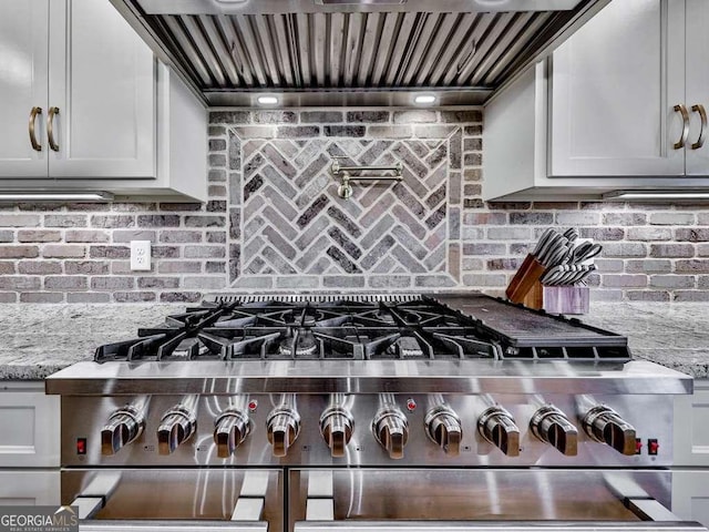 kitchen with light stone counters, wall chimney exhaust hood, high end stove, and backsplash