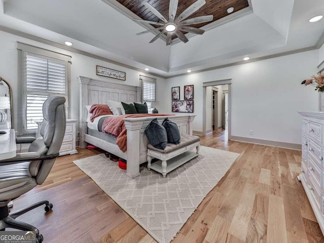 bedroom with ceiling fan, a tray ceiling, multiple windows, and light wood-type flooring