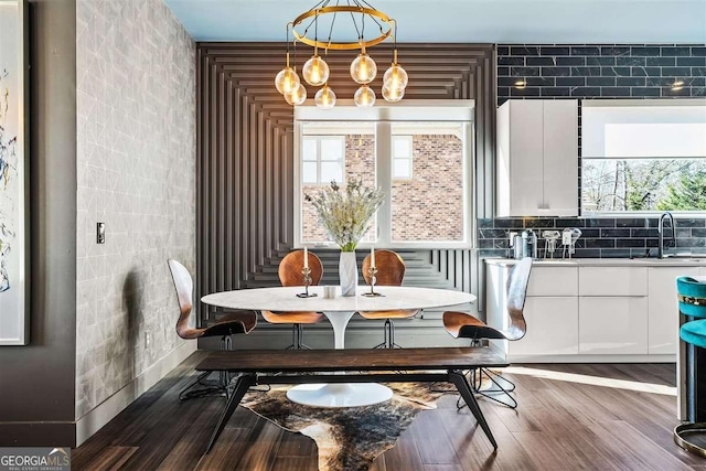 dining room with sink, an inviting chandelier, dark hardwood / wood-style flooring, and tile walls