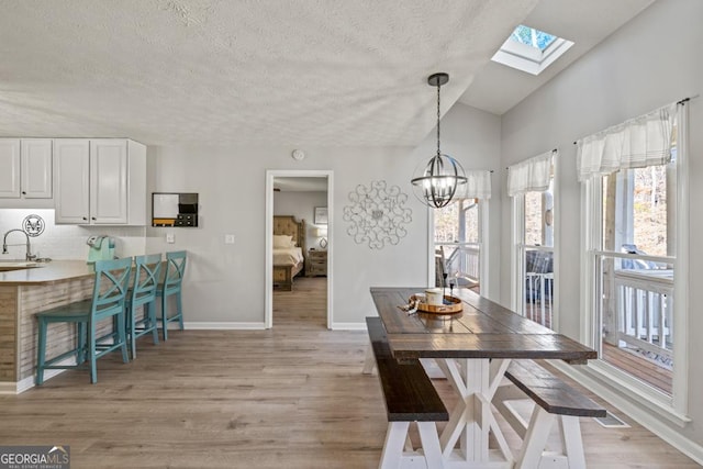 dining area with lofted ceiling, sink, a chandelier, a textured ceiling, and light hardwood / wood-style flooring