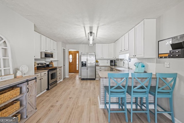 kitchen with a breakfast bar, appliances with stainless steel finishes, white cabinetry, light hardwood / wood-style floors, and kitchen peninsula