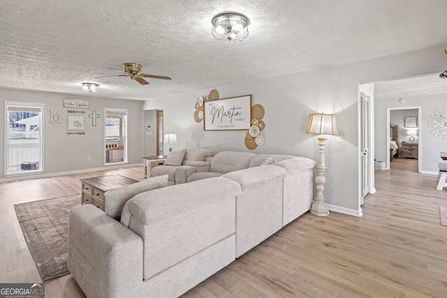 living room featuring ceiling fan, light hardwood / wood-style flooring, and a textured ceiling