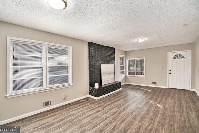 unfurnished living room with a brick fireplace, a textured ceiling, hardwood / wood-style floors, and a healthy amount of sunlight