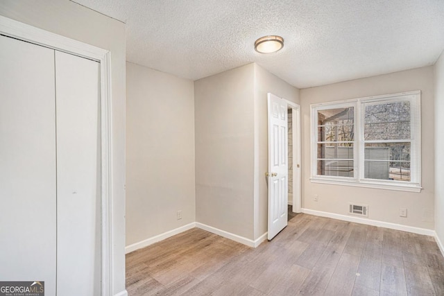 unfurnished bedroom featuring a closet, a textured ceiling, and light hardwood / wood-style flooring