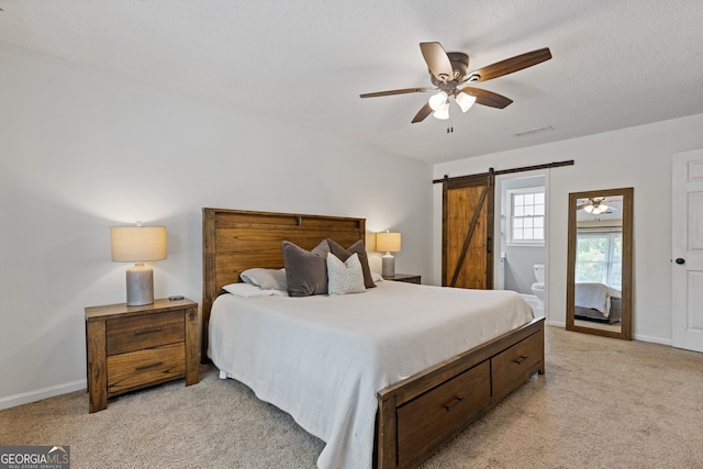 carpeted bedroom with a barn door, a textured ceiling, ceiling fan, and ensuite bath