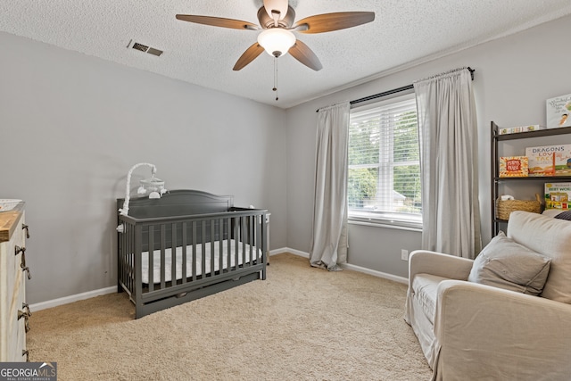 carpeted bedroom featuring ceiling fan, a crib, and a textured ceiling