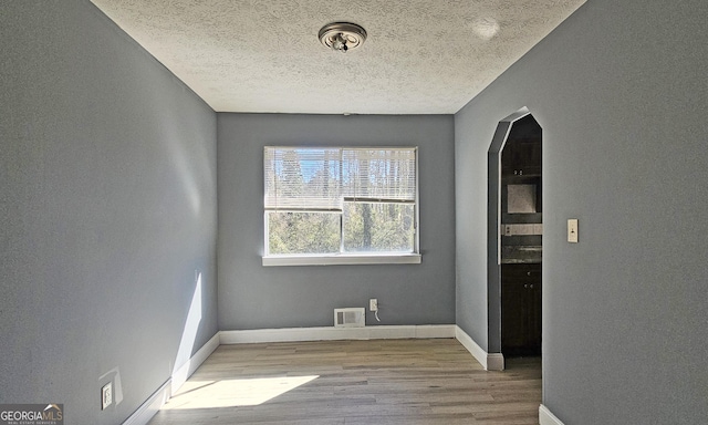 empty room with a textured ceiling and light hardwood / wood-style floors