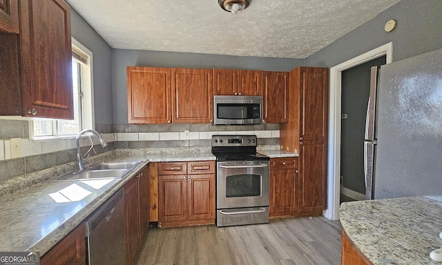 kitchen featuring appliances with stainless steel finishes, sink, a textured ceiling, and light wood-type flooring