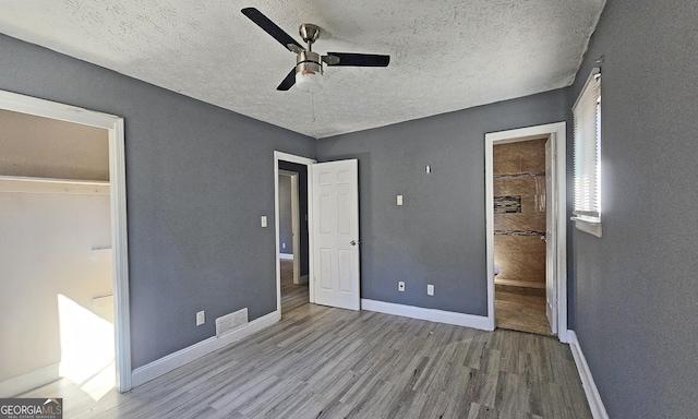 unfurnished bedroom featuring ceiling fan, connected bathroom, hardwood / wood-style floors, and a textured ceiling