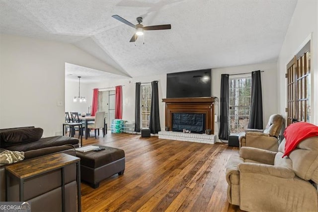 living room with vaulted ceiling, a fireplace, ceiling fan, dark wood-type flooring, and a textured ceiling