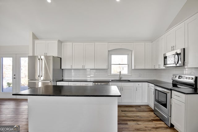 kitchen featuring vaulted ceiling, appliances with stainless steel finishes, sink, white cabinets, and a center island