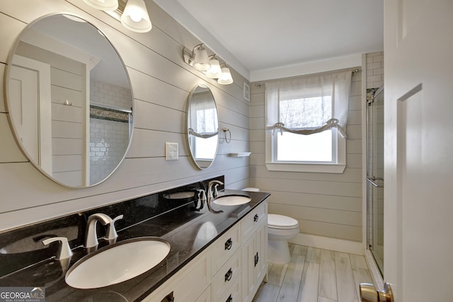 bathroom featuring hardwood / wood-style flooring, wooden walls, vanity, a shower with shower door, and toilet