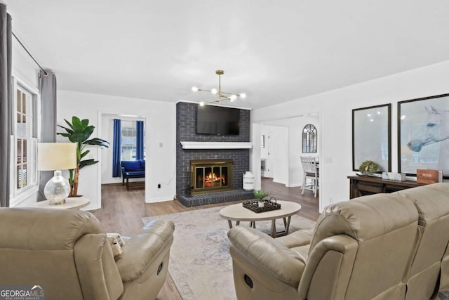 living room featuring an inviting chandelier, hardwood / wood-style floors, and a brick fireplace