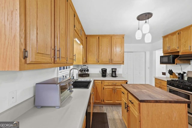 kitchen featuring sink, stainless steel gas range, a center island, light hardwood / wood-style floors, and decorative light fixtures