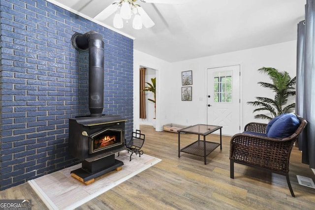 living room with brick wall, a wood stove, hardwood / wood-style floors, and ceiling fan