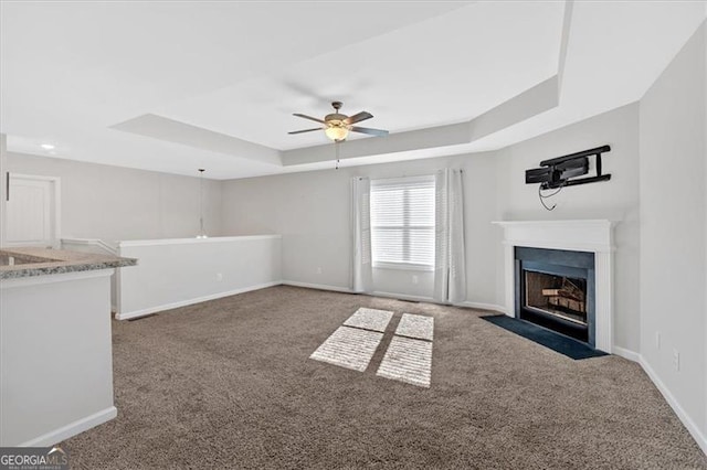 unfurnished living room with a tray ceiling, carpet floors, and ceiling fan